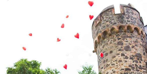 Brautpaar steht in Burghof und Ballons steigen in den Himmel